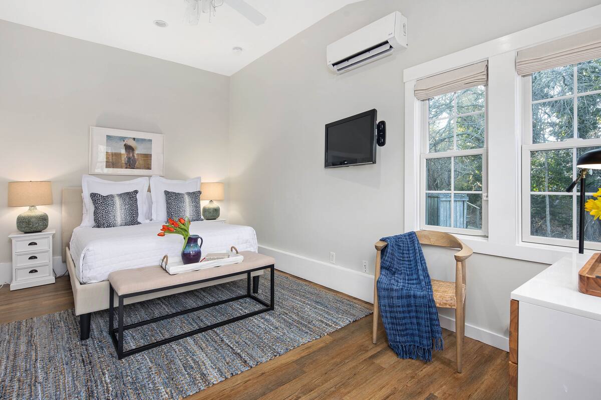 A bedroom with a bed, bedside tables, a TV, a window with a view, and a ceiling fan.