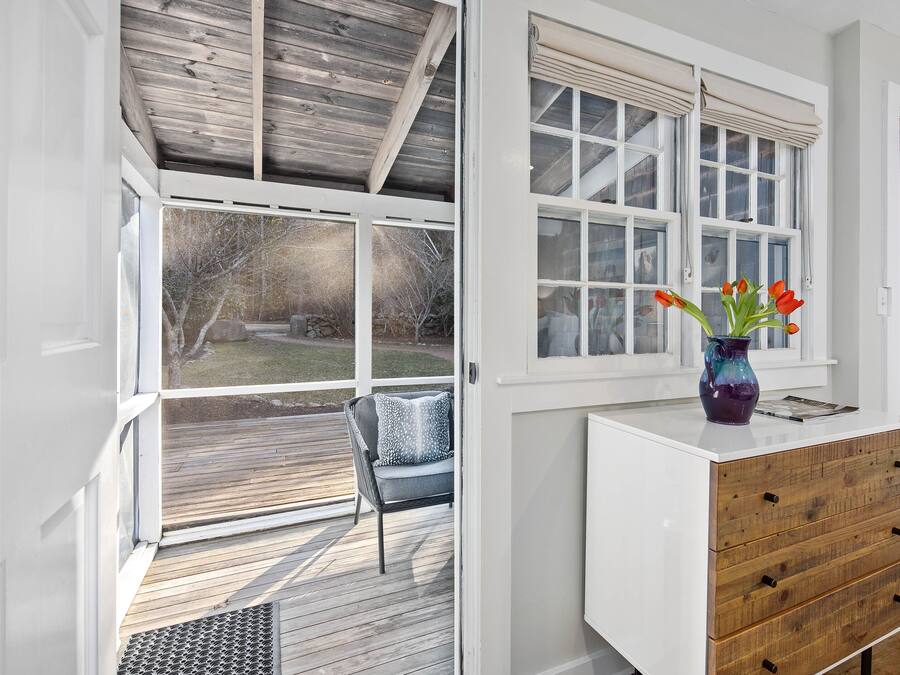Una habitación con terraza de madera, cómoda blanca y ventana con vista a un jardín.