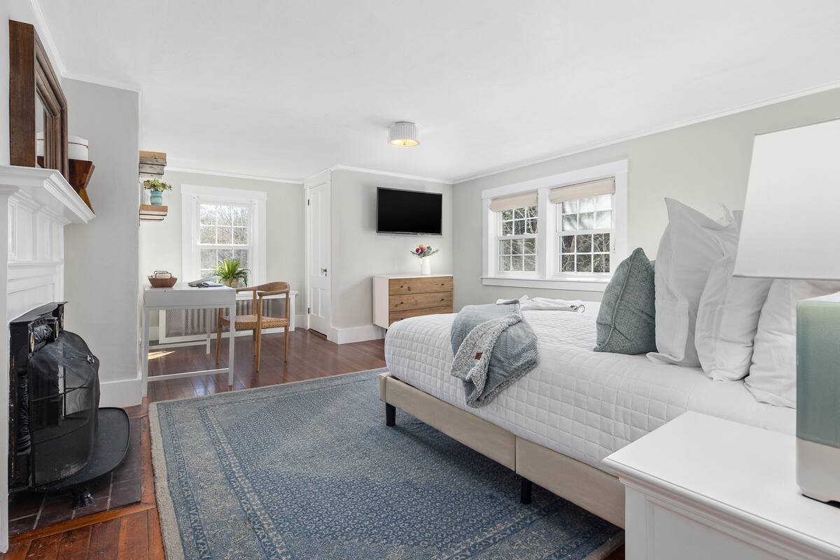 A bedroom with a bed, a TV, a fireplace, a desk, and a window.