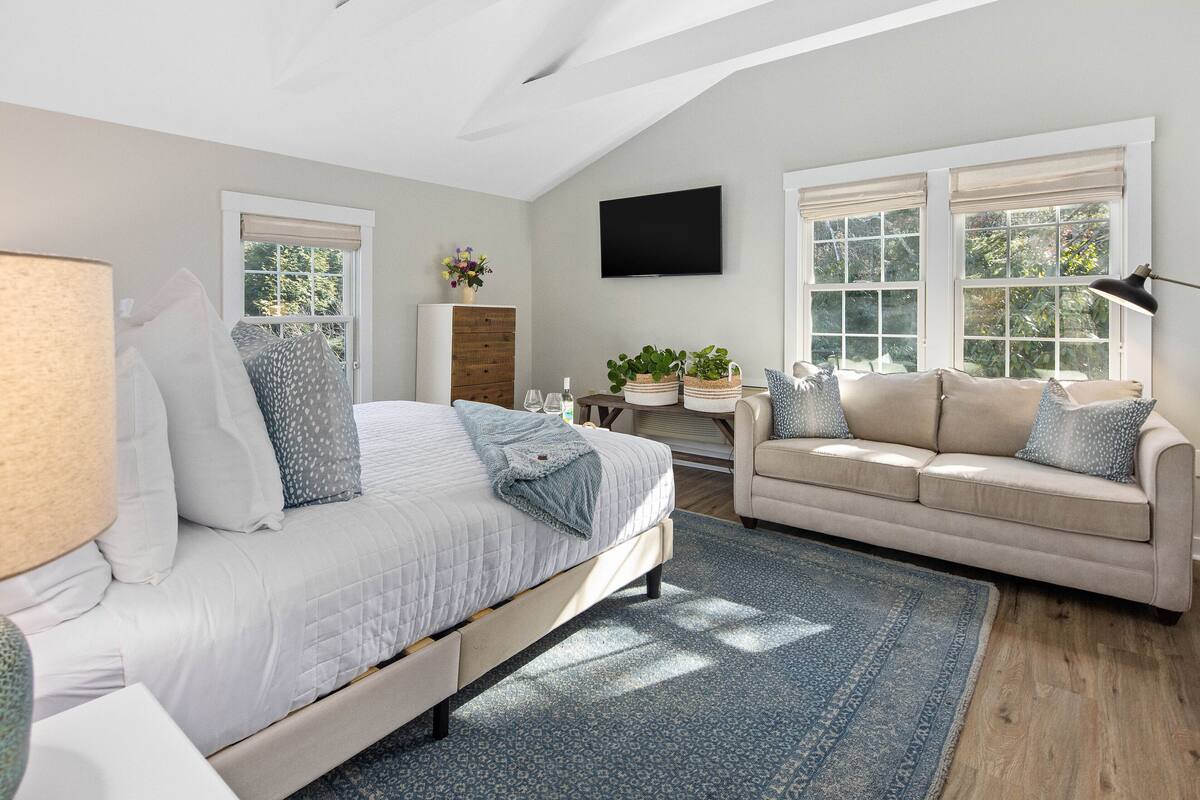 A bedroom with a bed, two sofas, a TV, and a window with a view of trees.