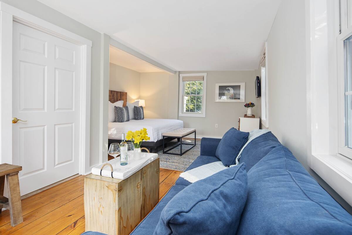 A room with a bed, a blue sofa, a wooden coffee table, and a window.