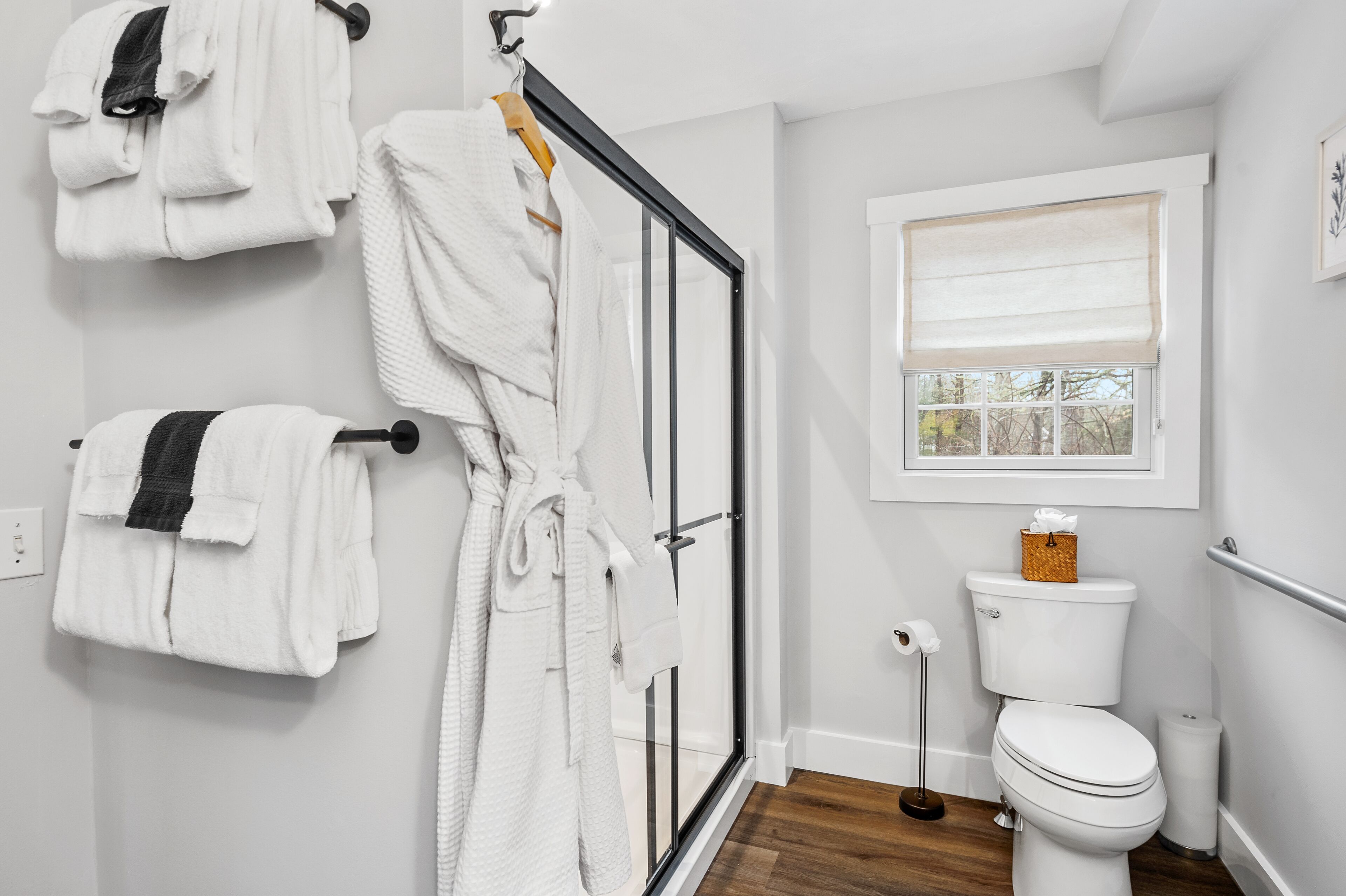 A bathroom with a glass shower door, a toilet, and a window with a blind.