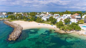 A coastal resort with clear turquoise waters, a sandy beach, and a row of white buildings with blue roofs. - Point Village Studios and Suites (Negril)