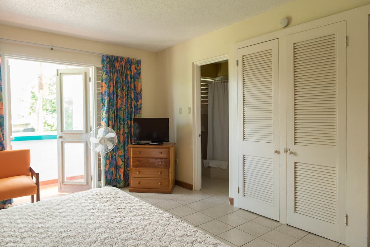 Ein Schlafzimmer mit Bett, Schminktisch, Fernseher, Ventilator und Kleiderschrank.