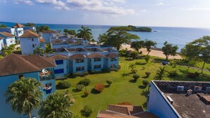 A resort with multiple blue buildings, a well-maintained lawn, and a beach view. - Point Village Studios and Suites (Negril)