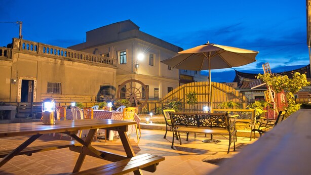 An outdoor dining area with tables and chairs, a large umbrella, and a building in the background. - Kinmen RuJia B&B (Jincheng)