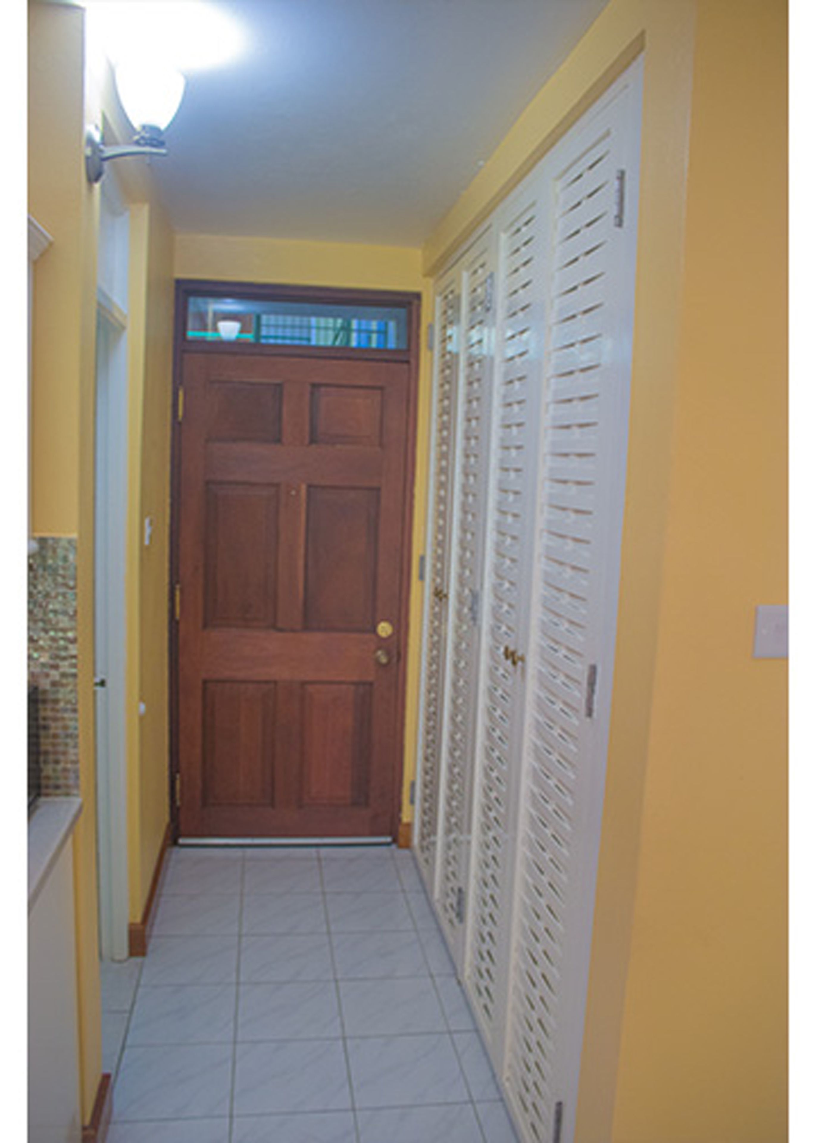 A narrow hallway with a wooden door and a white closet with louvered doors.