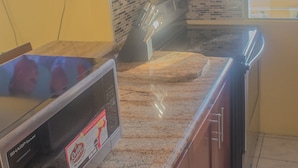 A kitchen with a granite countertop, a microwave, and a tiled backsplash. - Sand Dreams Beach at Turtle Towers (Ocho Rios)