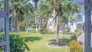 A well-maintained lawn with palm trees and a flower bed, surrounded by a building with large windows and a white exterior. - Conch Shell Beach Studio at Sandcastles Resort (Ocho Rios)