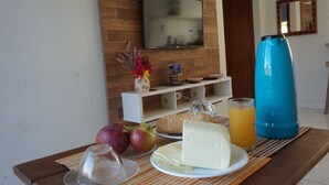 Une table dressée pour le petit-déjeuner, avec des fruits, du fromage et du jus, ainsi qu’une télévision et un miroir dans une pièce aux murs en bois.