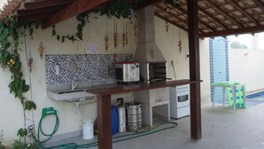 Une cuisine avec un mur recouvert de carreaux, une cuisinière à gaz, un four à micro-ondes et des plantes suspendues.