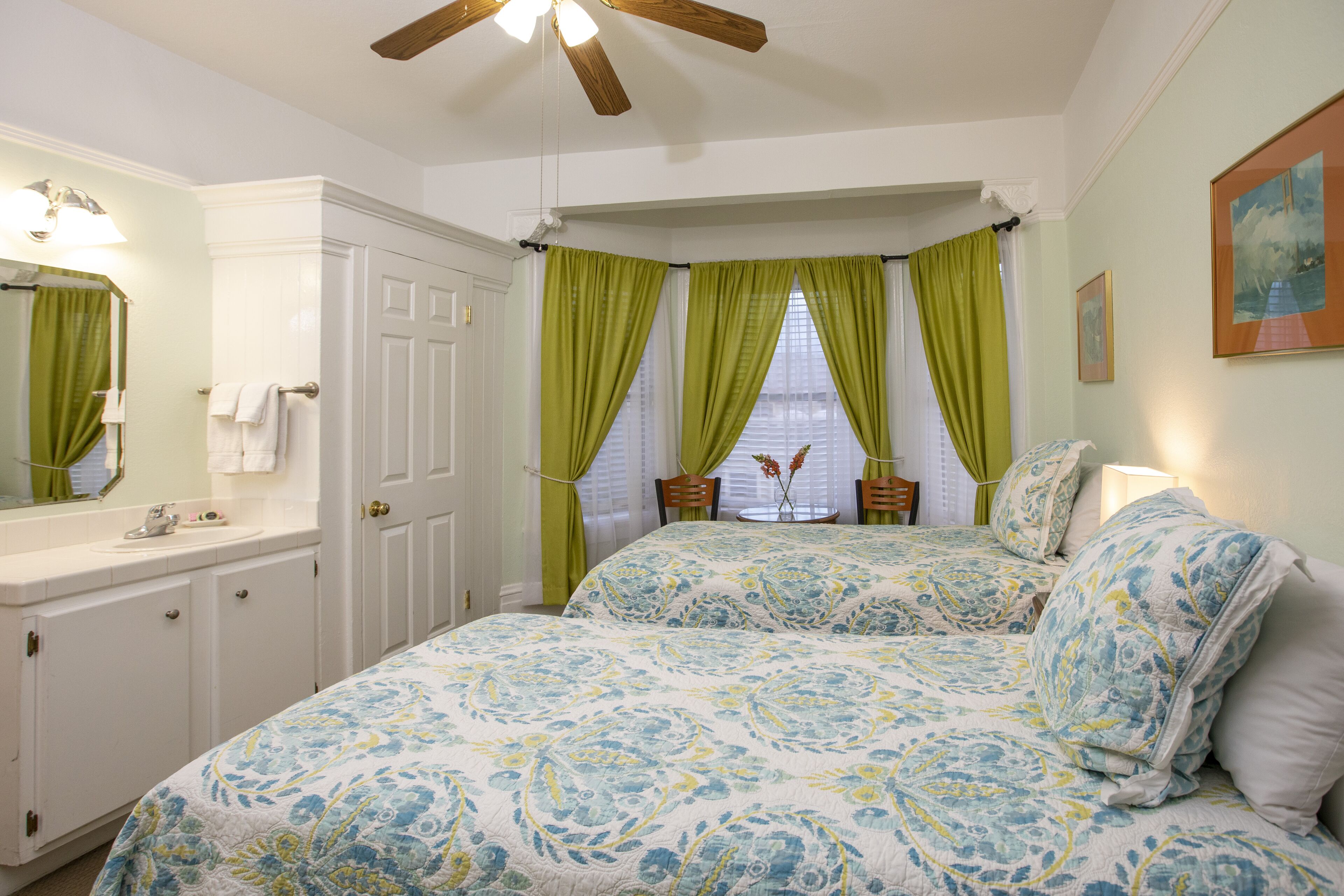 A bedroom with a large bed, a vanity with a mirror, and a window with green curtains.