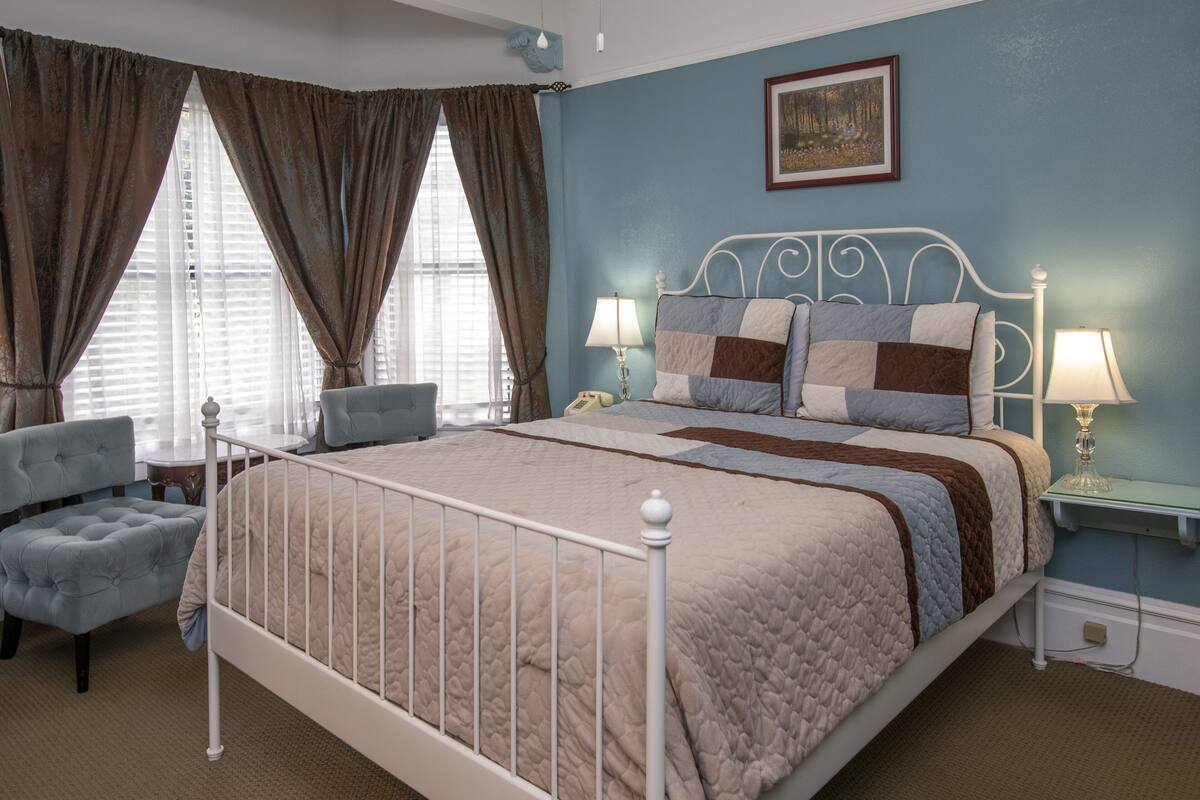 A bedroom with a bed, two bedside tables with lamps, a chair, and a window with curtains.