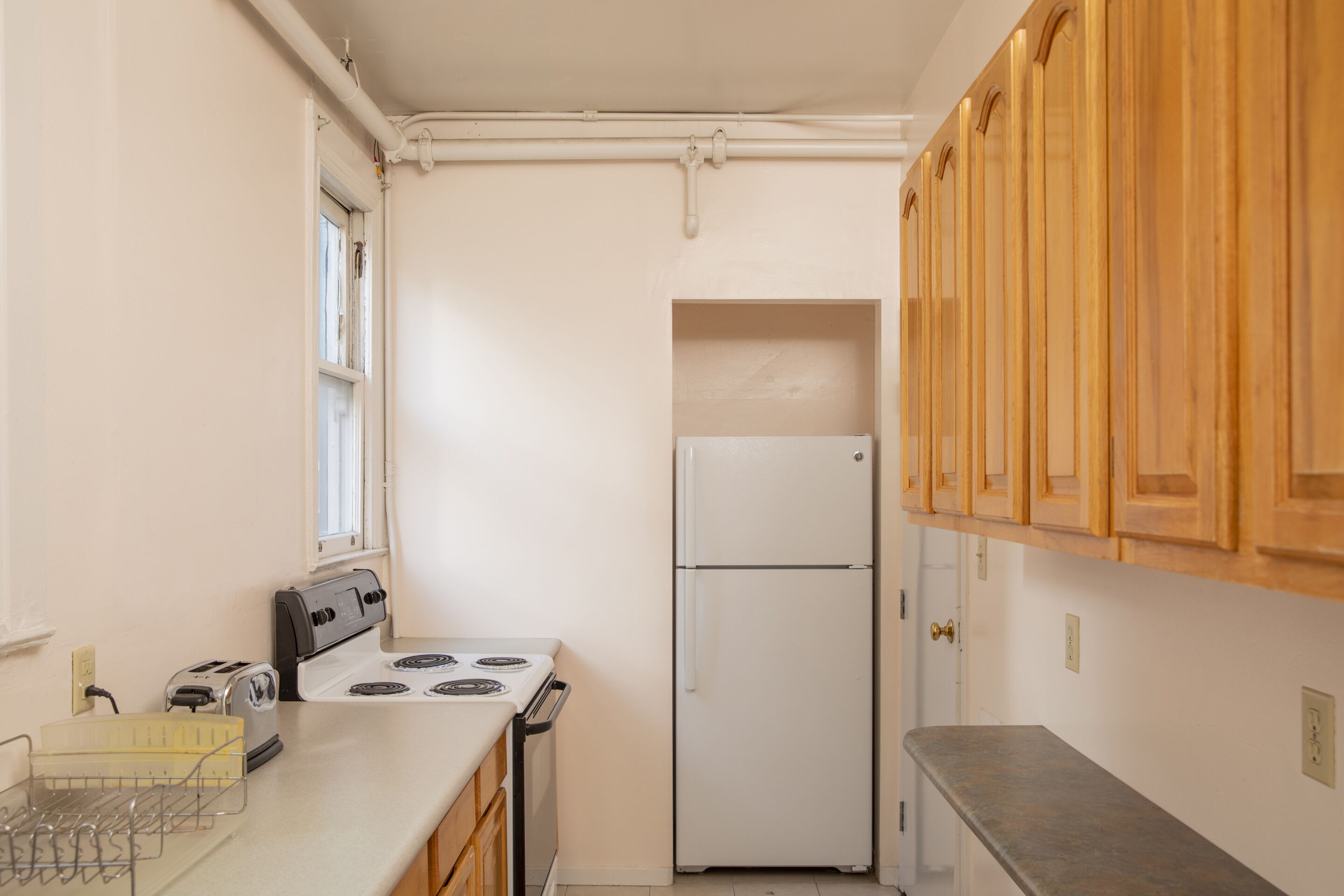A small kitchen with white appliances, wooden cabinets, and a window.