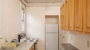 A small kitchen with white appliances, wooden cabinets, and a window.