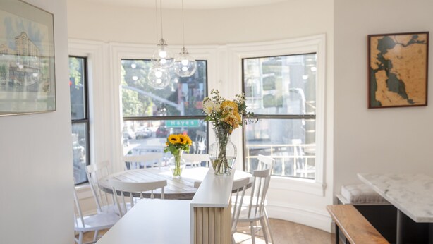 A dining area with a round table, white chairs, a bench, and a vase with flowers. - Hayes Valley Inn (San Francisco)