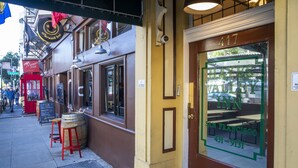 A hotel entrance with a glass door displaying the name "Hayes Valley Inn" and a phone number. There are outdoor tables and stools outside the entrance. - Hayes Valley Inn (San Francisco)