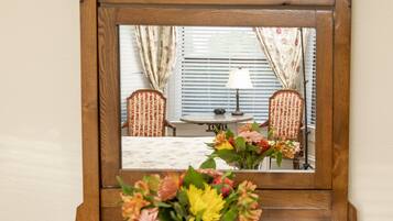 Un aparador de madera con un espejo arriba que refleja una habitación con una ventana, cortinas y una lámpara.