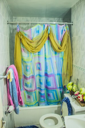 Un baño con cortina de ducha colorida, inodoro y lavamanos con una cesta decorativa.