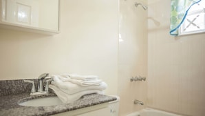 A bathroom with a sink, stacked towels, a shower, and a bathtub. - Island Blues Cottage at Draxhall Country Club (Ocho Rios)