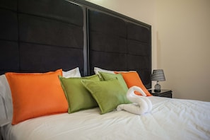 A neatly made bed with white bedding and multiple pillows in orange and green.