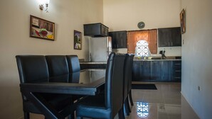 A dining area with a table and chairs, a kitchen with cabinets and a refrigerator, and a window with curtains. - Island Blues Cottage at Draxhall Country Club (Ocho Rios)