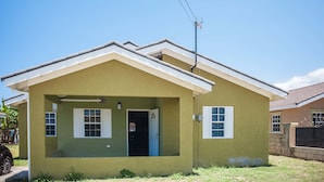 A single-story house with a gabled roof, a front porch, and a small front yard. - Island Blues Cottage at Draxhall Country Club (Ocho Rios)