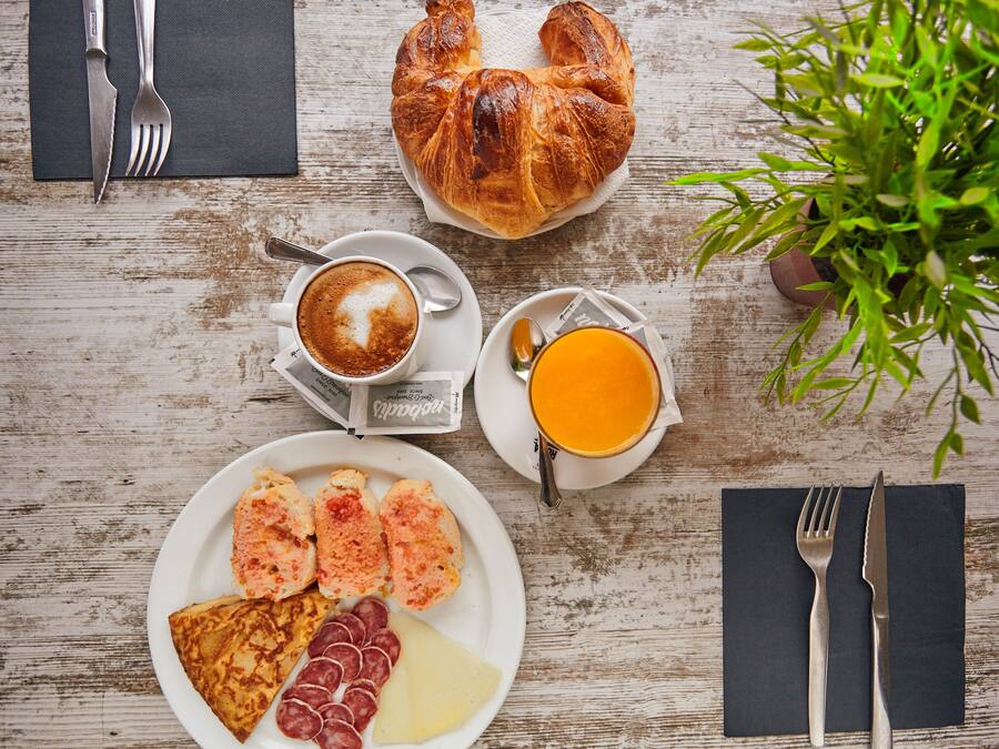 Disposição para o café da manhã com croissant, café, suco de laranja e diversos tipos de carne sobre uma mesa de madeira.