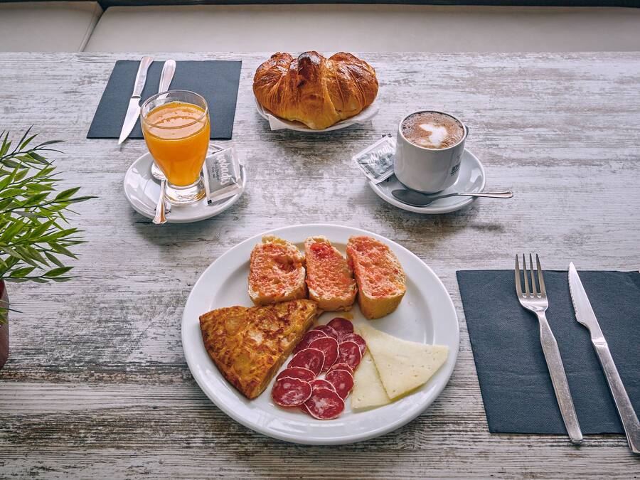 A breakfast setting with croissants, coffee, orange juice, and a plate of toast, ham, and cheese on a wooden table.