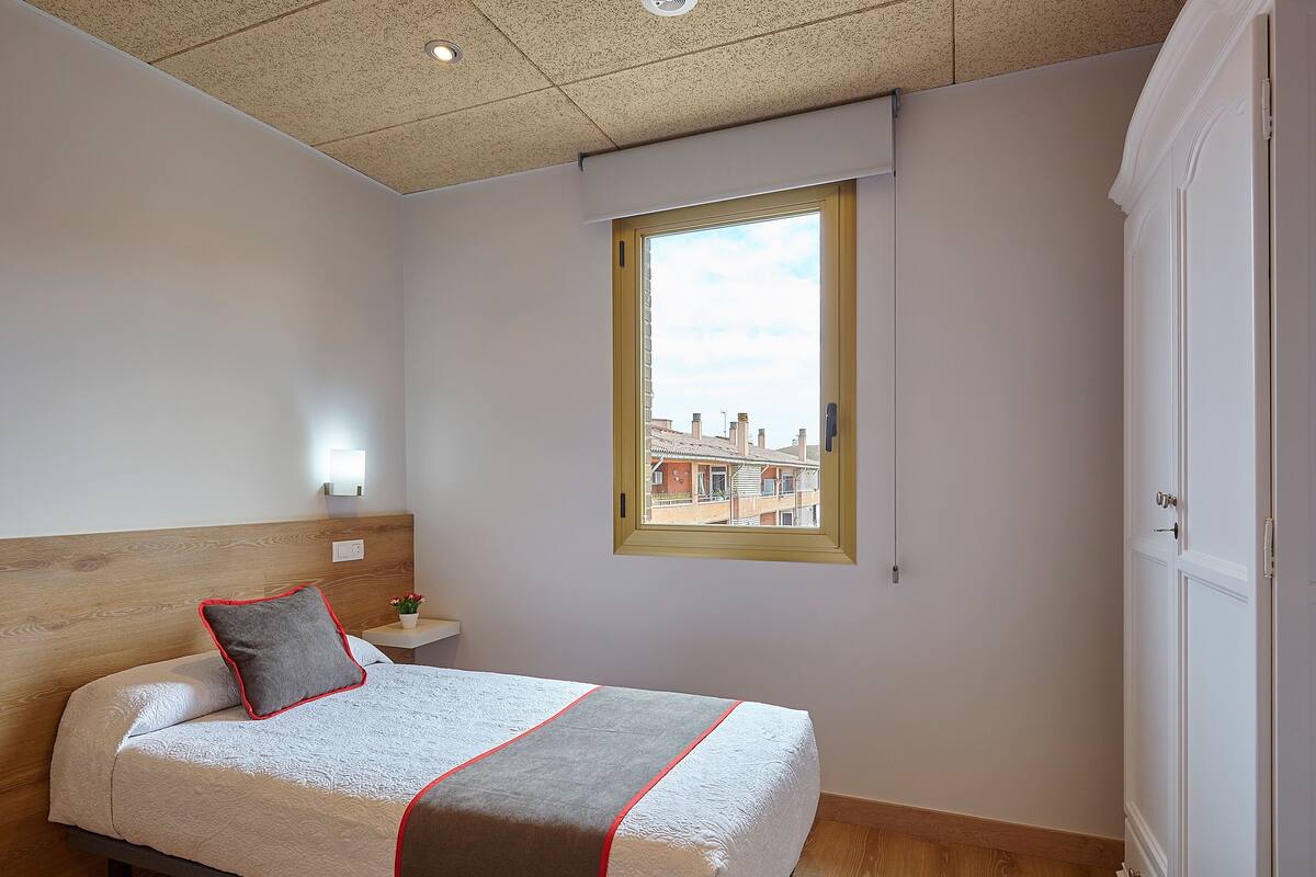 A bedroom with a bed, a nightstand, a window with a view, and a wardrobe.