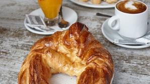 A croissant on a white napkin, a cup of coffee, and a glass of orange juice on a wooden table. - Hostal Nobadis (Cervera)