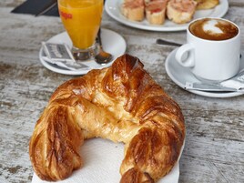 Un croissant sobre un mantel blanco, una taza de café y un vaso de jugo de naranja en una mesa de madera.