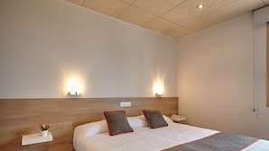 A neatly arranged bedroom with a wooden headboard, a bed with a white and grey bedspread, two bedside tables with lamps, and a small plant on one table. - Hostal Nobadis (Cervera)