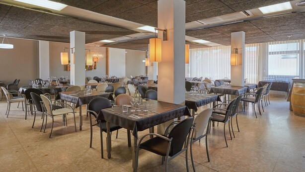 A spacious dining area with multiple tables and chairs, high ceilings with exposed beams, and large windows allowing natural light. - Hostal Nobadis (Cervera)