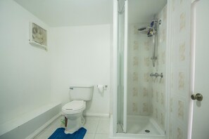A bathroom with a toilet, a shower with a glass door, and a blue bath mat. - Tall Palms (Montego Bay)