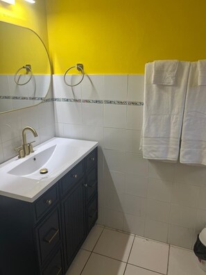 A bathroom with a white sink, dark cabinets, and yellow and white tiled walls. - Racquet Club (Montego Bay)