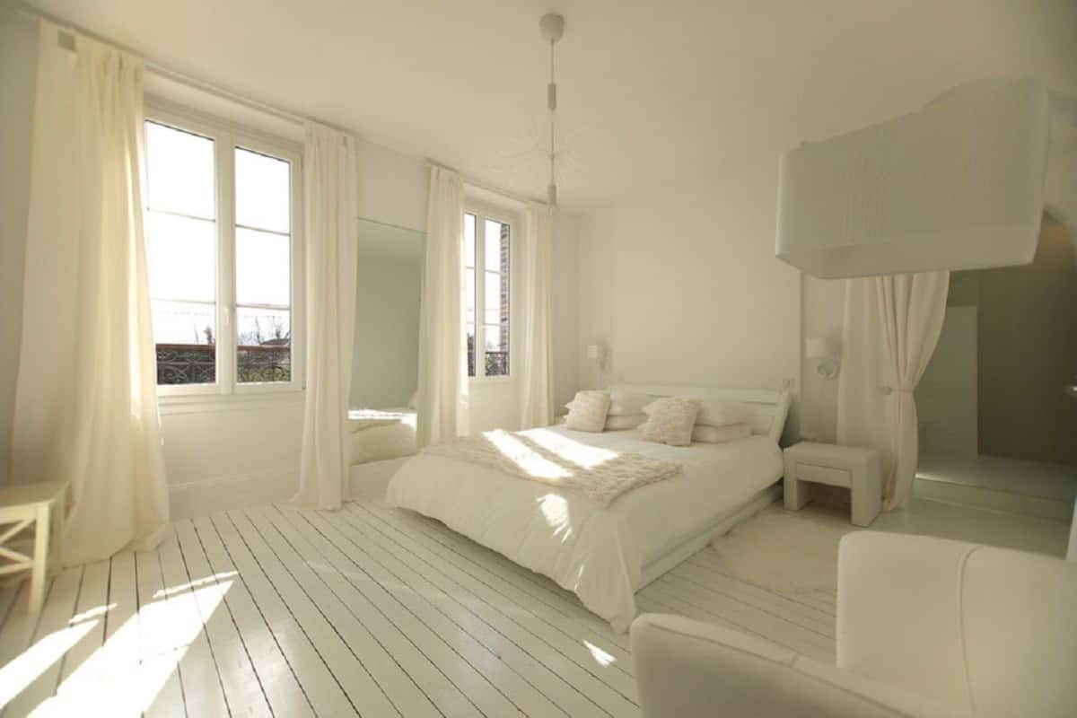 A bedroom with a large bed, a bedside table, a chair, and a window with curtains.