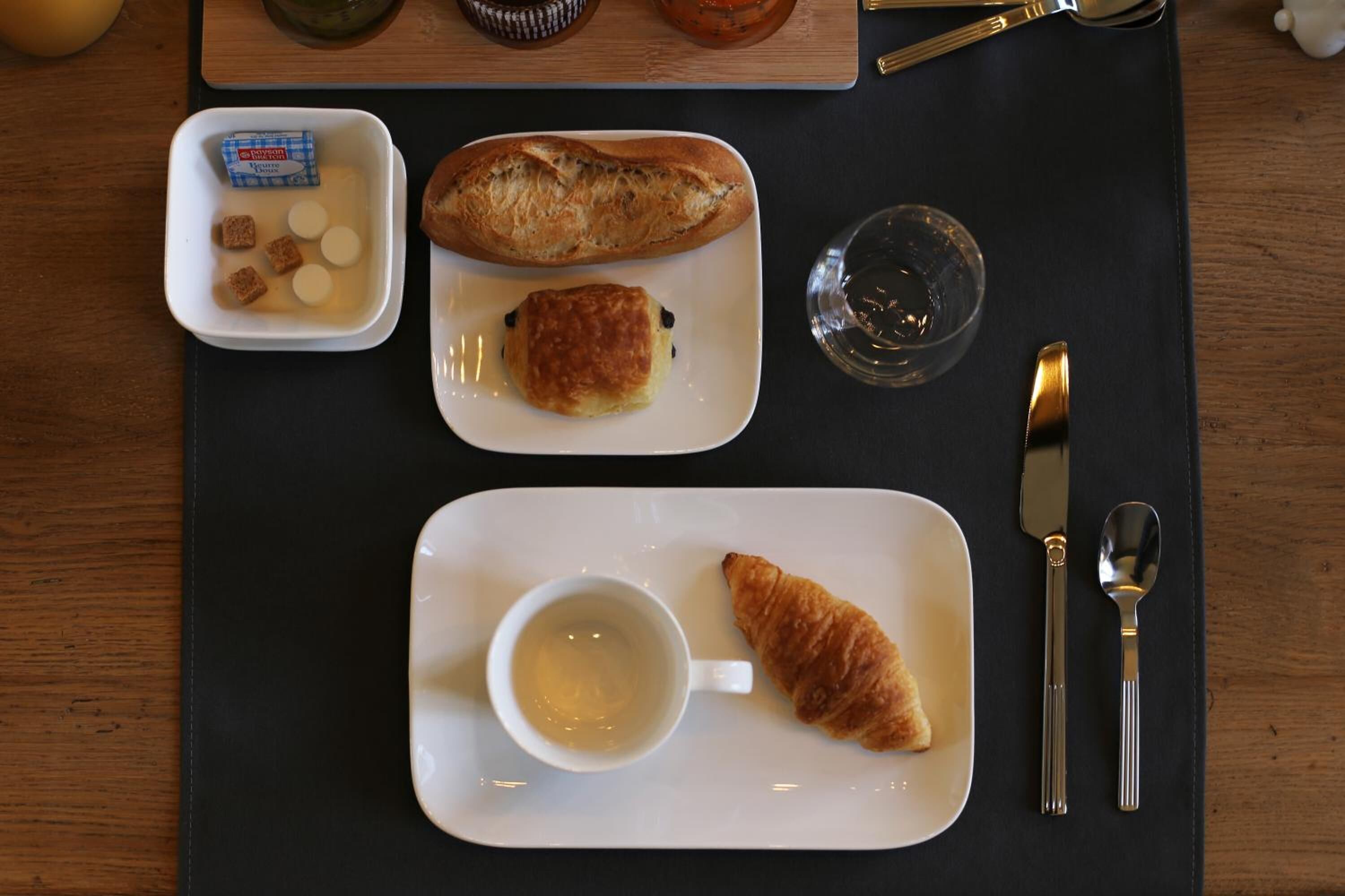 A breakfast setting with a croissant, a small pastry, and a cup of tea on a tray.