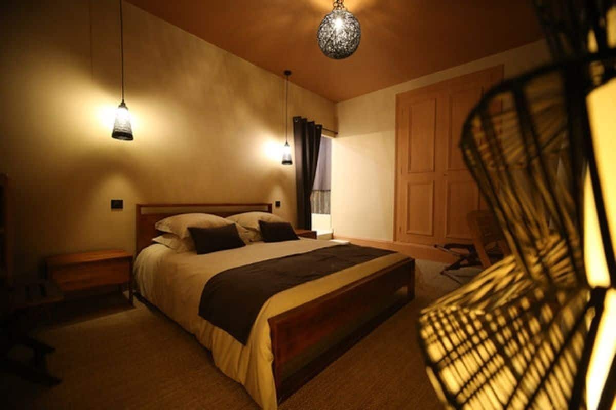A bedroom with a large bed, two bedside tables, a chair, and a hanging light fixture.