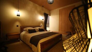 A bedroom with a large bed, two bedside tables, a chair, and a hanging light fixture.
