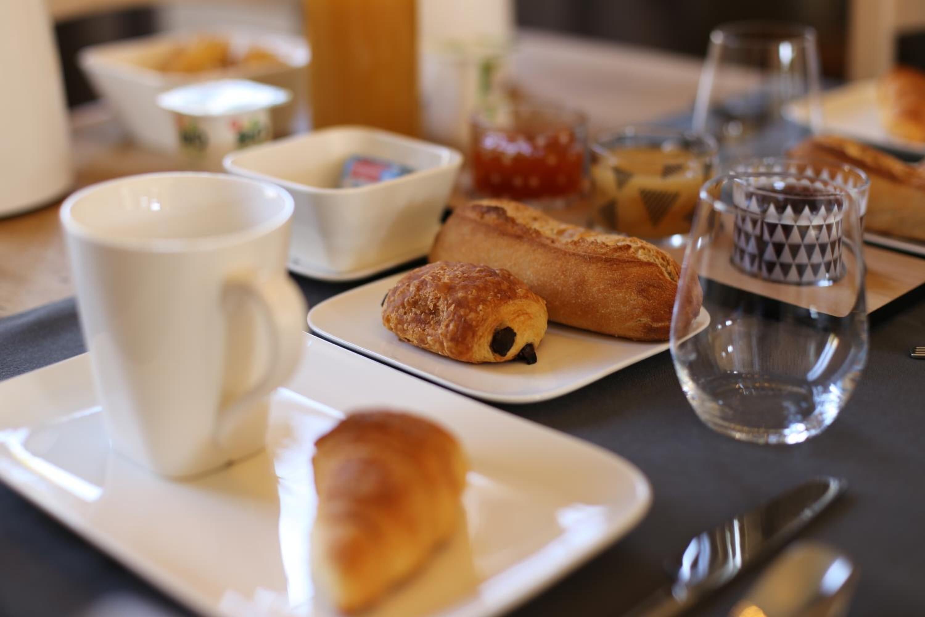 Een ontbijtsetting met croissants, een kop en een glas water op een tafel.
