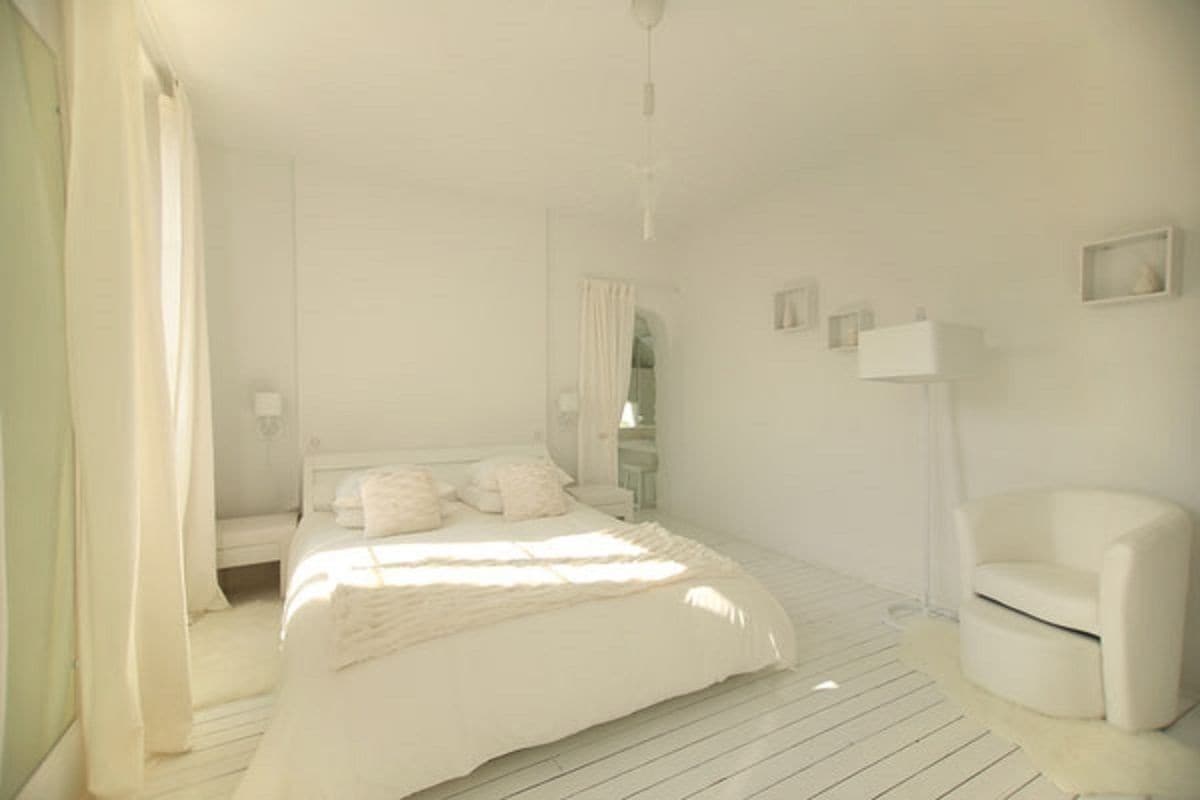 A minimalist bedroom with a large bed, a chair, and a bedside table.