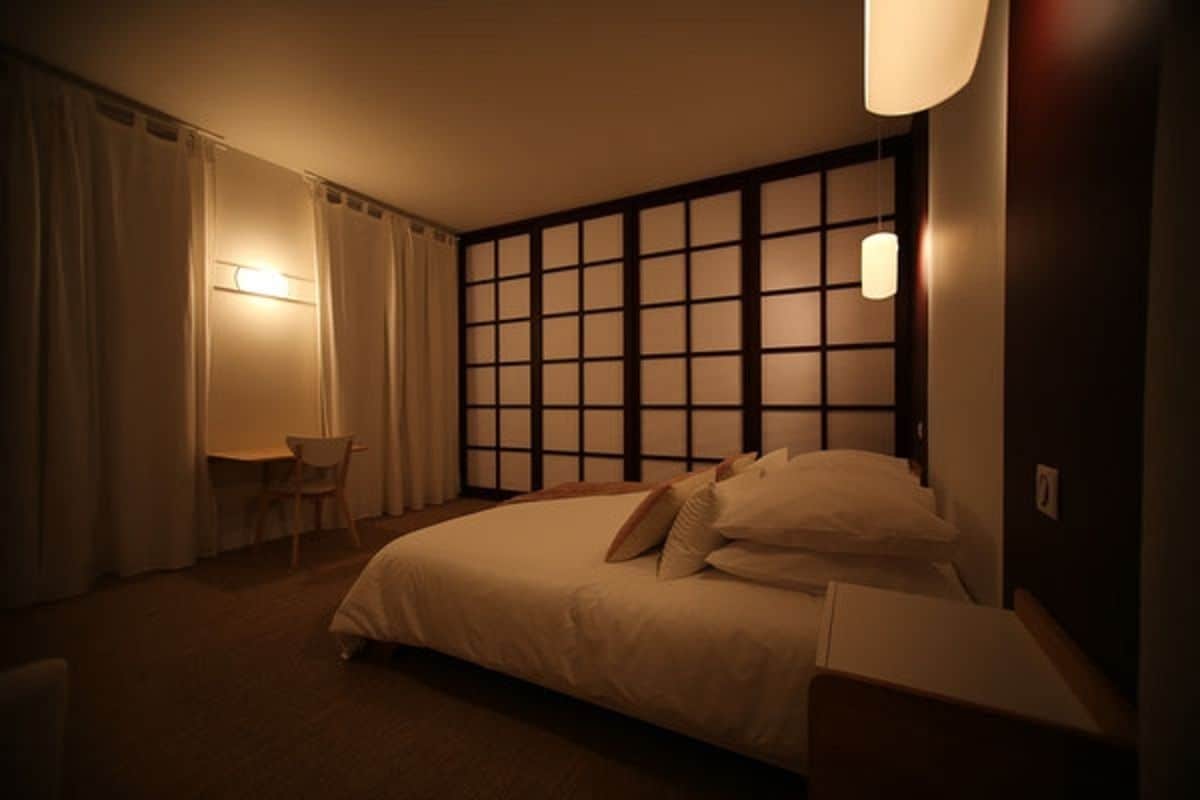 A hotel room with a large bed, a bedside table, a chair, and a wall with a grid pattern.