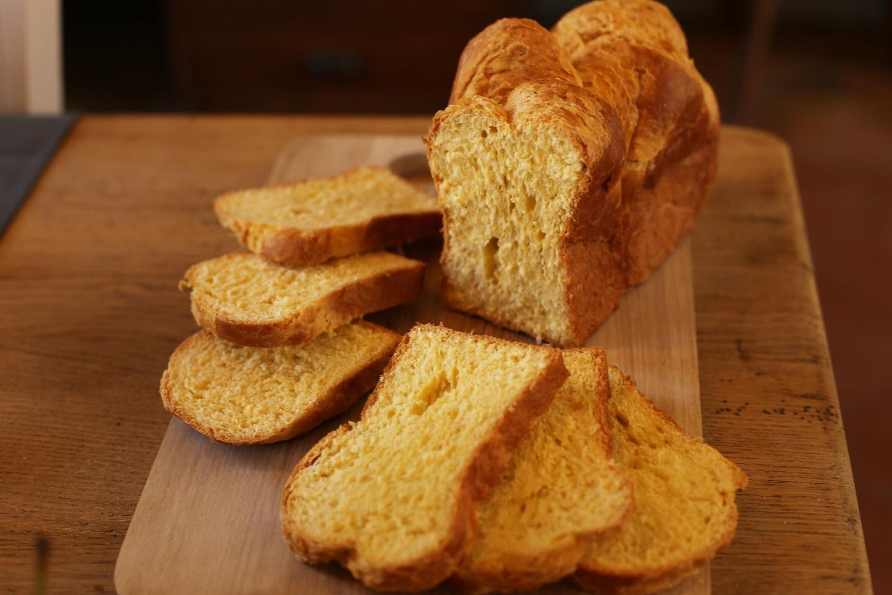 Een brood op een houten snijplank, waarvan enkele sneetjes zijn afgesneden.