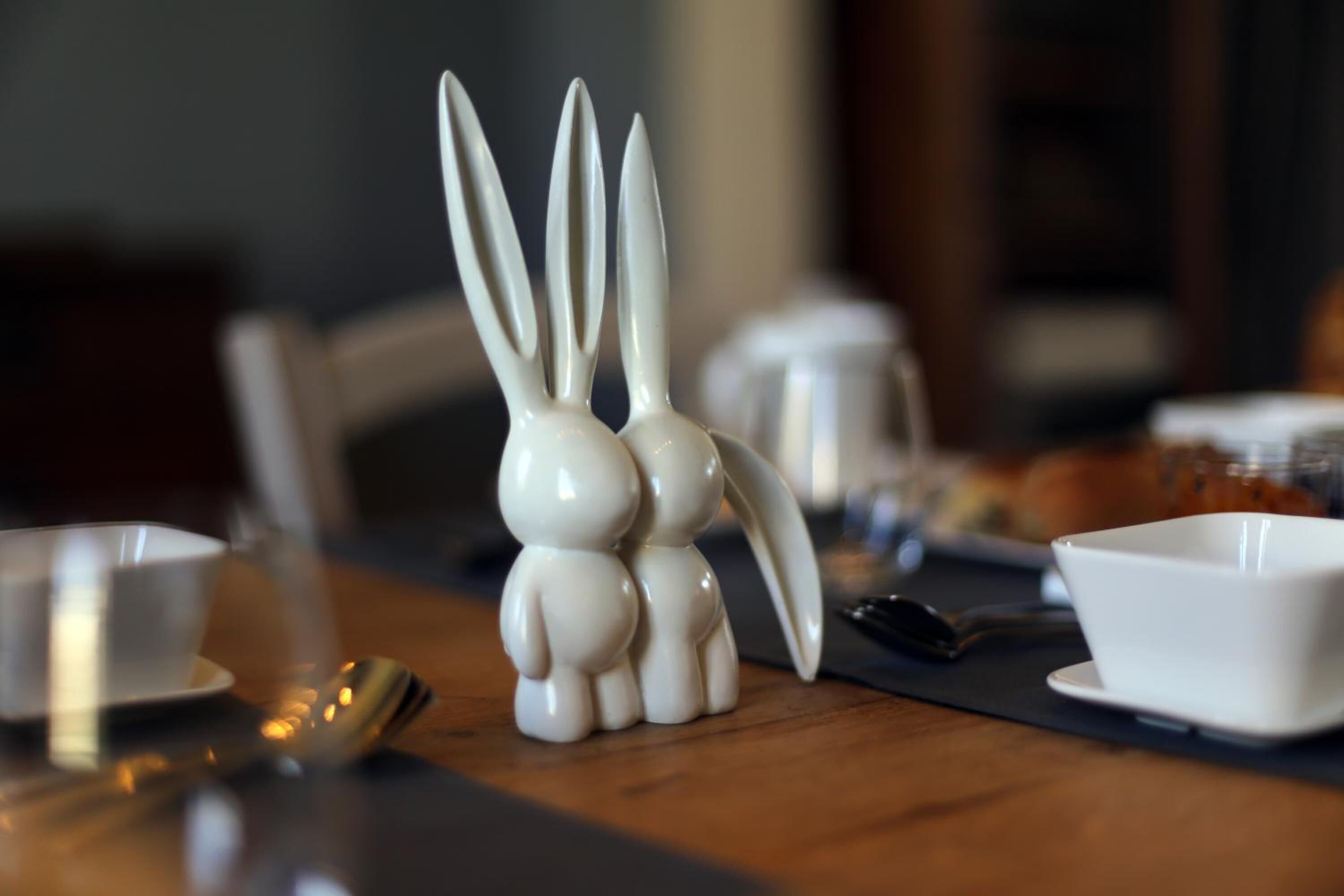 A table with a ceramic rabbit figurine, a white cup, a spoon, and a napkin.