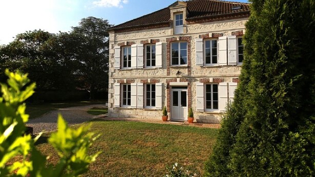 A two-story stone building with a tiled roof, a central entrance, and a small porch area.
