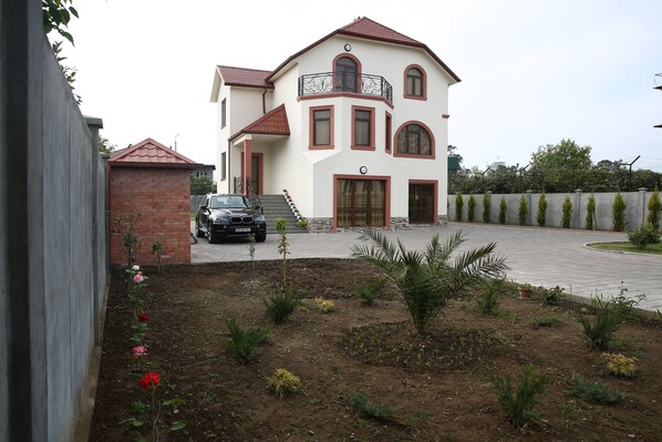 A two-story house with a red roof, a balcony, and a driveway leading to a parked car.