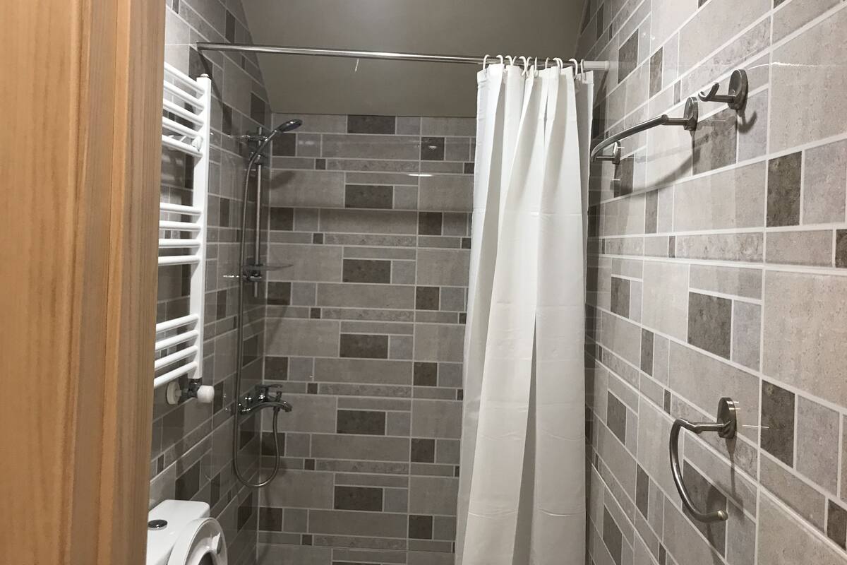 A shower with a glass door, tiled walls, and a white curtain.