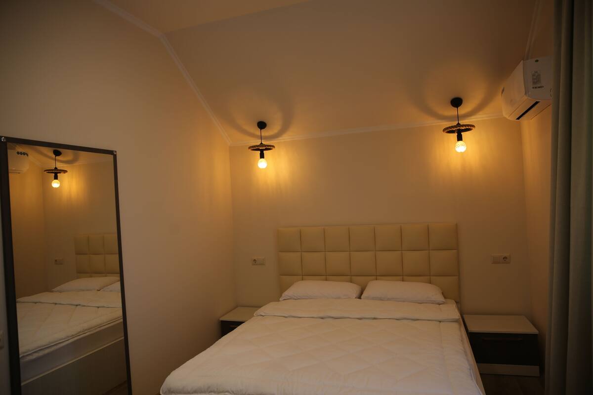 A bedroom with a bed, a nightstand, a mirror, and two wall-mounted lights.
