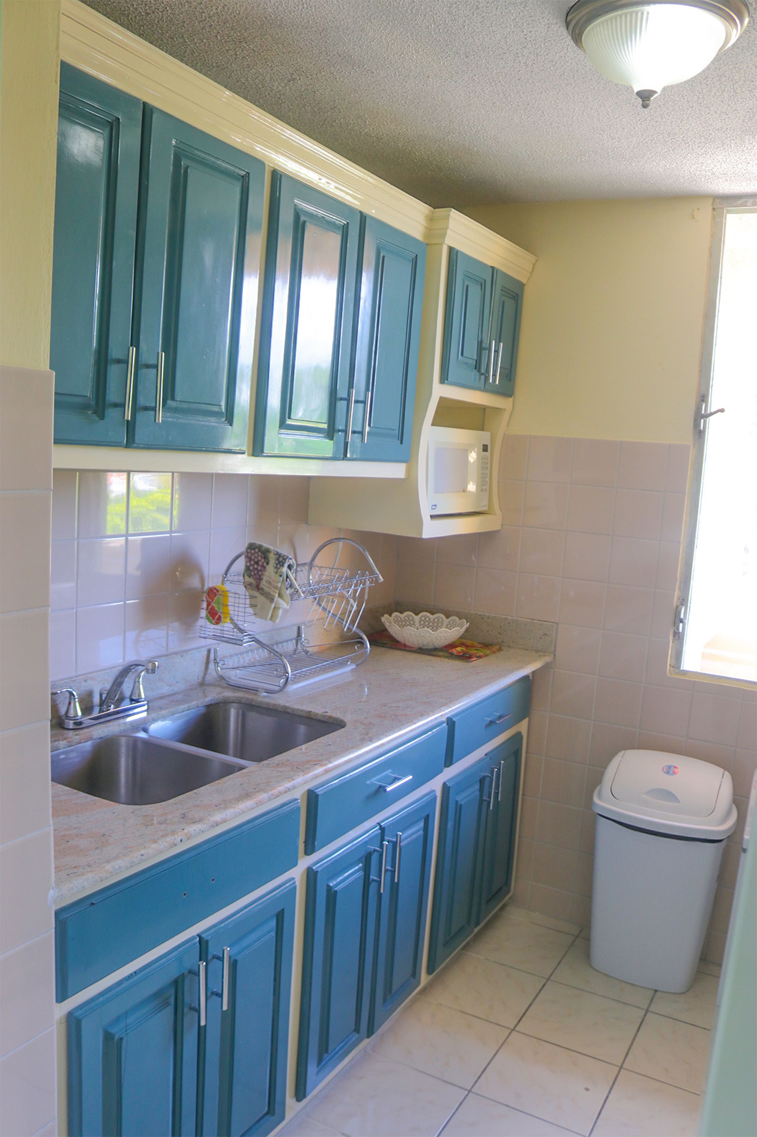 A kitchen with teal cabinets, a stainless steel sink, and a trash can.